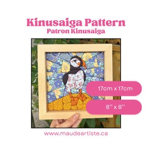 Peut inclure: Un motif Kinusaiga représentant un macareux fait de morceaux de tissu dans un cadre en bois clair. L'œuvre mesure 17cm x 17cm. Le macareux a un corps noir et blanc avec un bec et des pattes orange, sur un fond floral bleu et jaune.