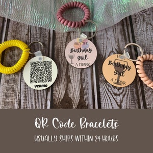 May include: Three colorful silicone bracelets with attached round tags. One tag has a QR code and the text "venmo". The other two tags have the text "Buy the Birthday girl a drink" with a wine glass icon.