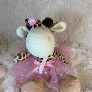 May include: A plush giraffe toy with a pink tutu and a pink flower on its head. The giraffe has brown spots and a cream-colored face. The feet are embroidered with "Flower Girl" and "Becca 07.15".