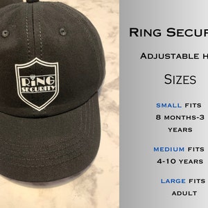 May include: Black adjustable baseball cap with a white logo that says "Ring Security". The logo is a shield with a crown on top. The hat is available in sizes small, medium, and large.