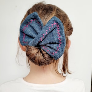 Peut inclure: Un nœud en jean bleu avec des coutures roses, porté en chignon.
