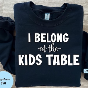 May include: Black sweatshirt with white text that reads "I belong -at the- kids table".