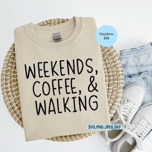 Puede incluir: Una camiseta beige con el texto "Weekends, Coffee, & Walking" impreso en negro. La camiseta se muestra en una cesta de mimbre con un par de zapatillas blancas y un par de vaqueros azules claros.