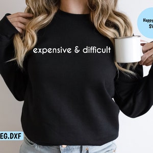 Könnte beinhalten: Ein schwarzer Pullover mit dem Aufdruck "expensive & difficult" in Weiß auf der Vorderseite. Der Pullover wird von einer Person getragen, die eine weiße Tasse hält.