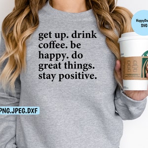 Puede incluir: Sudadera gris con el texto "get up. drink coffee. be happy. do great things. stay positive." Una persona sostiene una taza de café blanca con una manga de papel marrón.