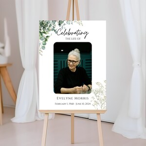 Pu&ograve; includere: Un poster commemorativo bianco con una foto di una donna, vegetazione verde e il testo "Celebrando la vita di Evelyne Morris, 1 febbraio 1968 - 10 giugno 2024".