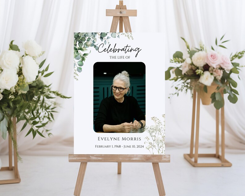 Pu&ograve; includere: Un cartello commemorativo bianco con un bordo floreale verde e una foto di una donna. Il cartello recita "Celebrating the Life of Evelyne Morris February 1, 1968 - June 10, 2024".