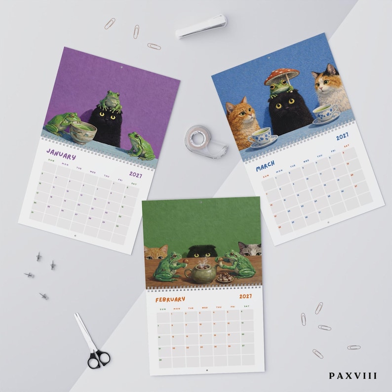 May include: A 2027 wall calendar featuring three pages for January, February, and March. Each page displays illustrations of cats and frogs in various settings, including tea parties and mushroom scenes, with a grid for dates and the text PAXVIII.