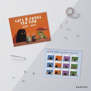 May include: A 2026-2027 wall calendar titled CATS & FROGS TEA TIME featuring a cover illustration of a black cat and a green frog with a mushroom umbrella at a table with tea cups, and a second page showing twelve monthly grid layouts.
