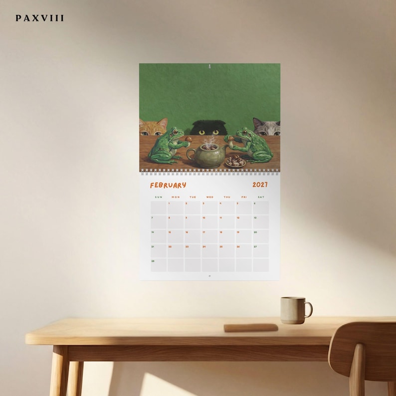 May include: A wall calendar for February 2027 featuring an illustration of two green frogs sitting at a table with a teapot and snacks, observed by three cats peering over the edge. The text PAXVIII is printed in the top left corner of the image.