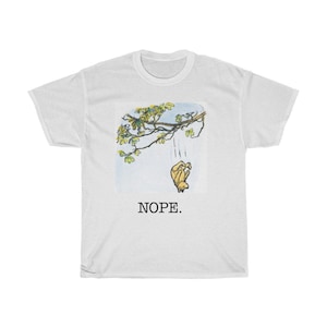May include: White t-shirt with a cartoon image of a bear falling from a tree branch. The text "NOPE." is printed below the image.