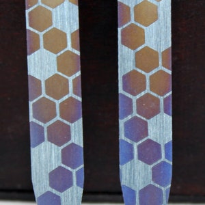 Puede incluir: Dos pasadores de corbata plateados con un patrón de panal. Los pasadores son un degradado de colores, comenzando con un marrón claro y pasando a un azul oscuro.
