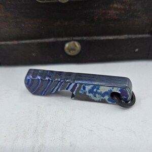 Puede incluir: Un abridor de botellas de metal con un patrón azul y morado con un llavero.