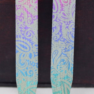 Puede incluir: Dos soportes de cuello plateados con un patrón de paisley y un degradado de colores de morado a azul.