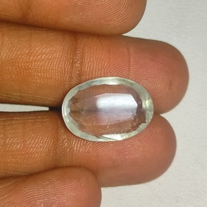 Può includere: Una gemma ovale e sfaccettata, di colore verde pallido. La gemma è tenuta tra le dita, mostrando la sua chiarezza e taglio. Adatta per gioielli.