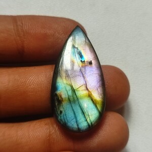 Pode incluir: Uma gema de labradorita em forma de lágrima com tons iridescentes azuis, verdes e roxos.