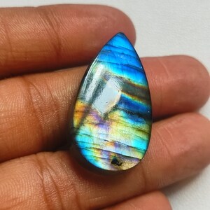 Pode incluir: Uma gema de labradorita em forma de lágrima com cores iridescentes azuis, verdes e douradas.