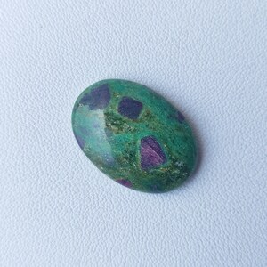 Könnte beinhalten: Ovaler Cabochon-Edelstein mit grüner Basis und Einschlüssen in Lila und Blau.
