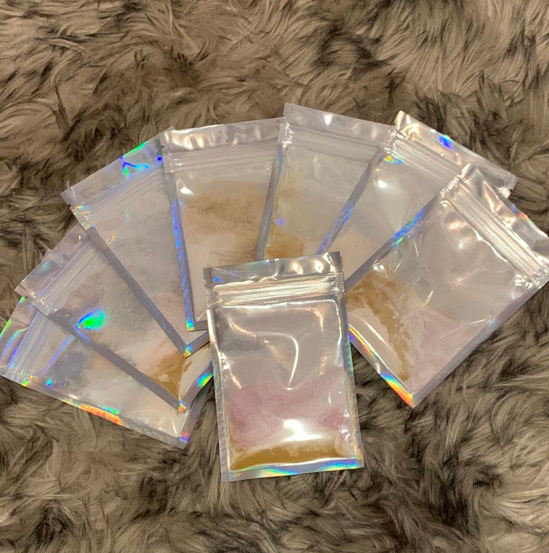 May include: Six clear plastic resealable bags with iridescent holographic foil accents, each containing a different colored powder. The powders are various shades of brown, pink, and purple.