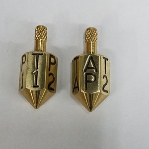 May include: Two gold-colored metal spinning tops with black lettering. The tops have six sides with the letters "T", "A", "P", and "1", "2", "P" on one top and "T", "A", "P", and "1", "2", "T" on the other.