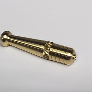 May include: A gold-colored metal pipe with a rounded end and a textured section. The pipe is about 4 inches long.