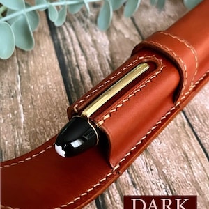 May include: A brown leather pen case with a dark honey finish. The case has a flap that closes with a snap. A black and gold pen is inside the case.