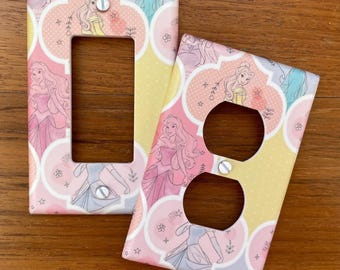May include: Two decorative light switch and outlet covers featuring a pastel pink, yellow, and blue pattern with illustrations of Disney princesses. The covers have a Moroccan-inspired design with a repeating pattern of princesses in their gowns.