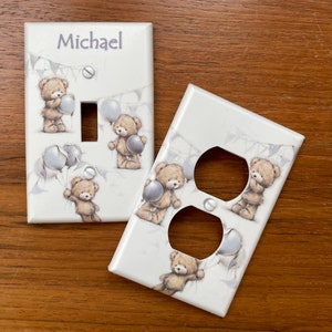 May include: Two white light switch and outlet covers with a teddy bear and balloon design. The light switch cover has the name Michael on it.