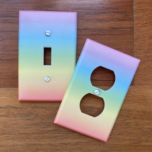 May include: Two rainbow-colored light switch and outlet covers. The switch cover has a single switch and the outlet cover has a standard double outlet.