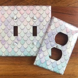 May include: Two light switch and outlet covers with a mermaid scale pattern in shades of pink, purple, and blue.