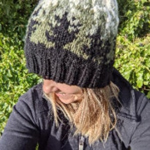 May include: A black, green, and white knit hat with a gradient pattern. The hat has a cable knit design and a pompom on top.