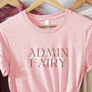 Op de afbeelding: Roze T-shirt met de tekst "ADMIN Fairy" in bruine letters.