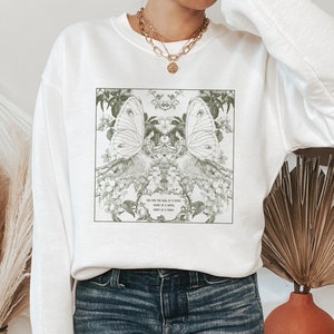 May include: White sweatshirt with a graphic print of two butterflies and floral designs. The text on the graphic reads "One who has the soul of a butterfly, never truly belongs in a frame."
