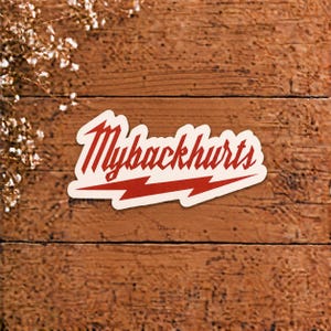 以下が含まれることがあります： 太字の赤いスタイリッシュなフォントで「Mybackhurts」というテキストが書かれたダイカットステッカー。文字は赤い稲妻のグラフィックの上に配置されており、デザイン全体がクリーム色の背景と縁取りで構成されています。
