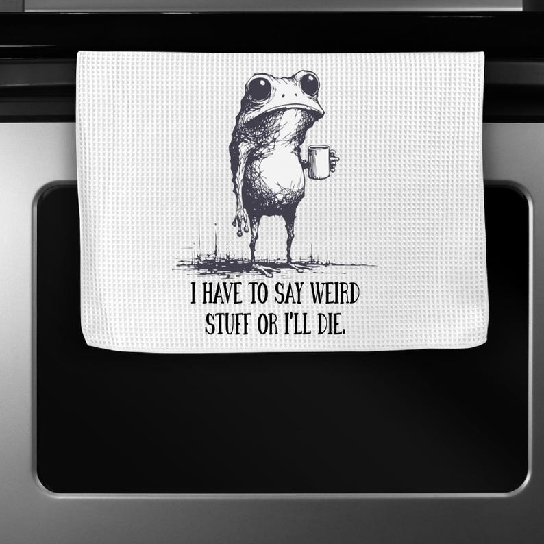 May include: White kitchen towel with a whimsical illustration of a frog holding a mug. The frog is drawn in black and white with large eyes. Text on the towel reads, "I HAVE TO SAY WEIRD STUFF OR I'LL DIE."