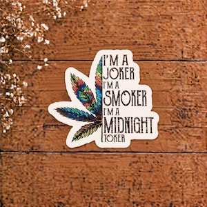 May include: A die-cut sticker featuring a multi-colored leaf design on the left side and the black text I'M A JOKER I'M A SMOKER I'M A MIDNIGHT TOKER on the right side. The leaf is composed of vibrant rainbow-colored feathers in a fan shape.