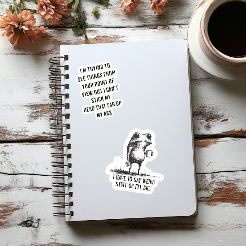May include: A spiral-bound notebook with a white cover featuring two stickers and text. One sticker shows a frog holding a mug, and the other has the text: "I'M TRYING TO SEE THINGS FROM YOUR POINT OF VIEW BUT I CAN'T STICK MY HEAD THAT FAR UP MY ASS."