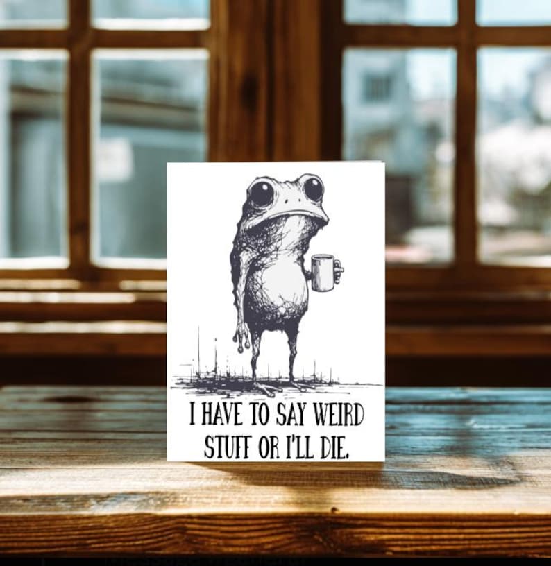 May include: A black and white illustration of a frog holding a mug. The frog has large eyes and a grumpy expression. The text "I HAVE TO SAY WEIRD STUFF OR I'LL DIE." is below the frog.
