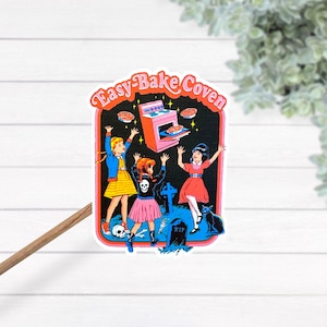 May include: A sticker with the text "Easy-Bake Coven" features three girls celebrating around a pink oven. The girls are wearing dresses and skirts, with a skull on one girl's shirt. A black cat and tombstone are also in the image.