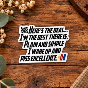 Könnte beinhalten: Ein weißer, konturgestanzter Aufkleber mit einem schwarzen Zielflaggen-Symbol und dem schwarzen Text: Here's the deal... I'm the best there is. Plain and simple I wake up and piss excellence. Der Aufkleber enthält eine kleine gelb-rot-blaue Streifengrafik.
