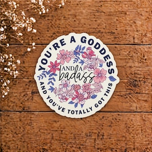 Può includere: Un adesivo circolare con sfondo color crema caratterizzato da una ghirlanda floreale di fiori rosa e viola. Il testo in blu scuro e nero recita: YOU'RE A GODDESS AND A BADASS AND YOU'VE TOTALLY GOT THIS. L'adesivo ha un bordo smerlato.