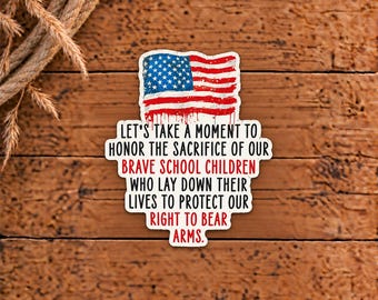 May include: A die-cut sticker featuring a distressed American flag graphic at the top. The text reads: LET'S TAKE A MOMENT TO HONOR THE SACRIFICE OF OUR BRAVE SCHOOL CHILDREN WHO LAY DOWN THEIR LIVES TO PROTECT OUR RIGHT TO BEAR ARMS.