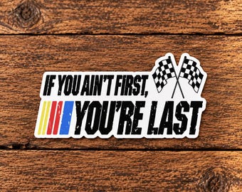 Può includere: Un adesivo rettangolare con il testo nero IF YOU AIN'T FIRST, YOU'RE LAST. Il design include due bandiere da corsa a scacchi bianchi e neri incrociate e una serie di strisce verticali gialle, rosse e blu sul lato sinistro dell'adesivo.