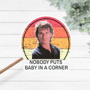 May include: A round sticker with a retro sunset design featuring a man with long hair. The sticker has the text "Nobody puts baby in a corner" printed below the image.