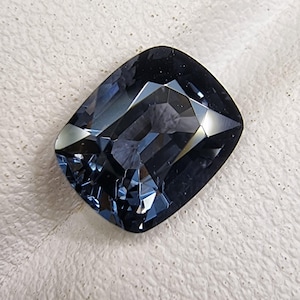 Peut inclure: Une pierre précieuse bleu foncé taillée en coussin avec une surface facetée.