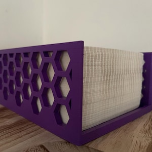 Puede incluir: Porta pañuelos de color morado con un patrón de panal de abeja. El porta pañuelos está hecho de madera y tiene una caja de pañuelos blanca en su interior.