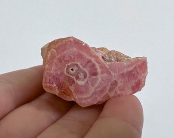 May include: A pink and white crystal with a swirling pattern. The crystal is a raw, unpolished piece with a natural shape.
