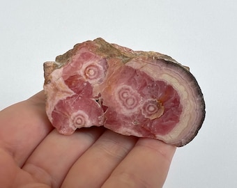 May include: A pink and brown, naturally formed, polished,  crystal with a circular pattern. The crystal is a raw, rough, and natural specimen.