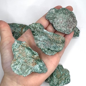May include: A collection of five green and brown rough, natural, unpolished, raw, tumbled, and uncut green serpentine stones.