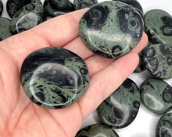 May include: A collection of polished green and black ocean jasper stones. The stones are smooth and have a swirling pattern.